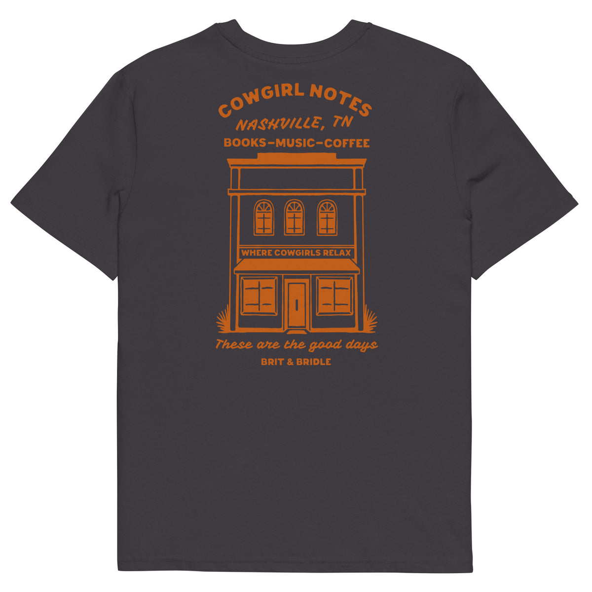 A dark charcoal gray t-shirt shown from the back, featuring a prominent orange graphic print of a vintage building with the text 'COWGIRL NOTES NASHVILLE, TN BOOKS-MUSIC-COFFEE' and 'These are the good days BIT & BRUISE'.