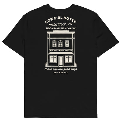 A black short-sleeve t-shirt with a white graphic print on the front depicting a storefront building and text reading 'COWGIRL NOTES NASHVILLE, TN BOOKS - MUSIC - COFFEE' and 'These are the good days BRIT & BRIDLE'.