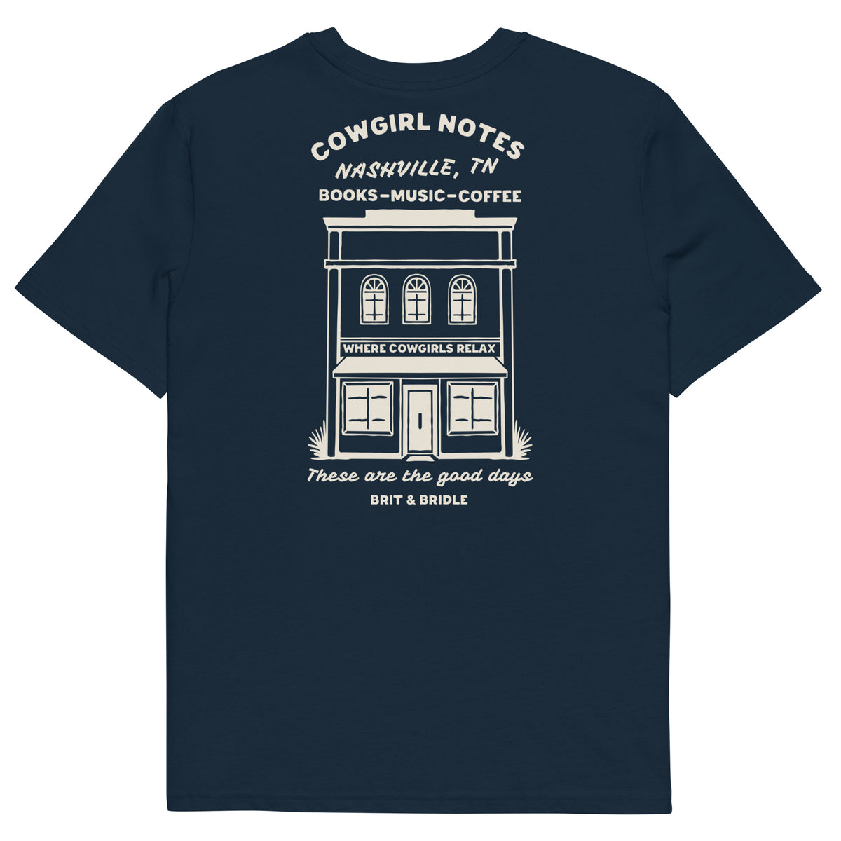 A navy blue short-sleeve t-shirt with a white graphic print on the front depicting a storefront and text reading 'COWGIRL NOTES NASHVILLE, TN BOOKS - MUSIC - COFFEE' and 'These are the good days BRIT & BRIDLE'.