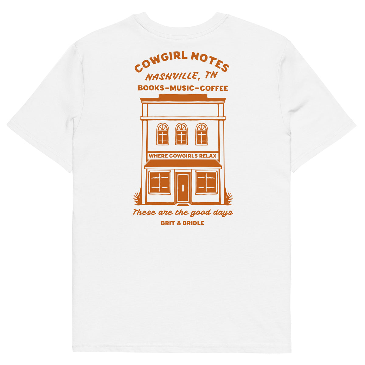 A white short-sleeve t-shirt with a retro-style orange graphic on the front. The graphic features a two-story building illustration with the text 'COWGIRL NOTES NASHVILLE, TN BOOKS-MUSIC-COFFEE' above it, and 'These are the good days BINT & BRIDLES' below it.